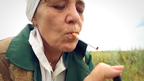 Aged Woman Smoking a Cigarette In a Scarf On The alt