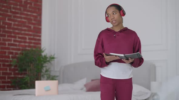 Young Professional African American Woman in Headphones Walking in Bedroom Talking Persuading