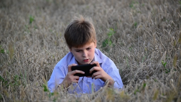 Teenage Boy Uses a Smartphone In Meadow In The