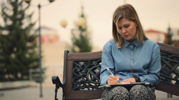 Girl Sitting On a Wooden Bench, Writes a Notebook