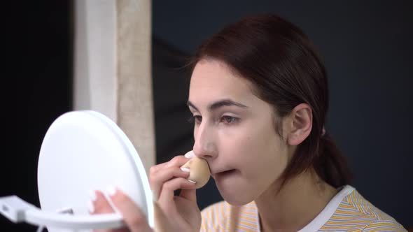 A Young Woman Looks Into a Small Mirror and Applies Makeup with a Sponge. Skin Care.