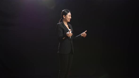Smiling Asian Speaker Woman In Business Suit Showing Thumbs Up Gesture In The Black Screen Studio