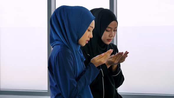 Two Asian Muslim young women in traditional hijab are praying glorify Allah