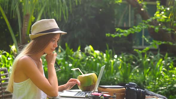 Blonde Woman Wearing Straw Hat and Working at Tropical Place and Drink Coconut