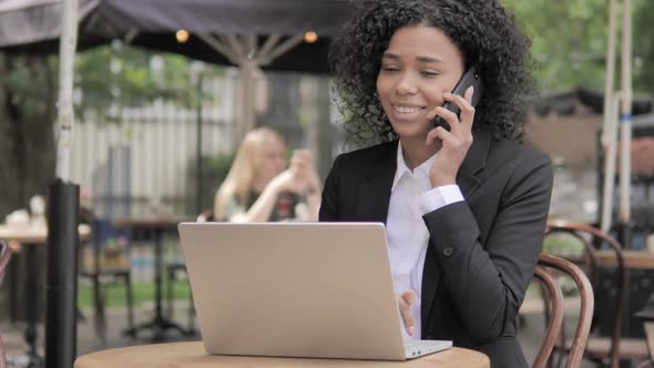 African Businesswoman Talking on Phone While Sitting in Outdoor Cafe