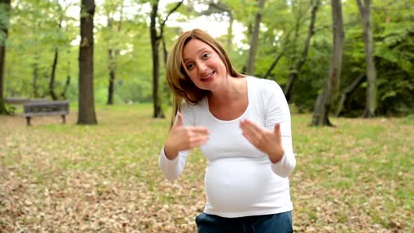 Young Pretty Pregnant Woman Invite People with Hands in Park