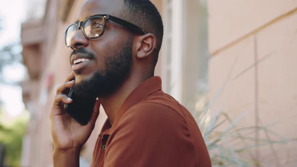 Cheerful Afro-American Man Chatting on Phone on Outdoor Coffee Shop Bench