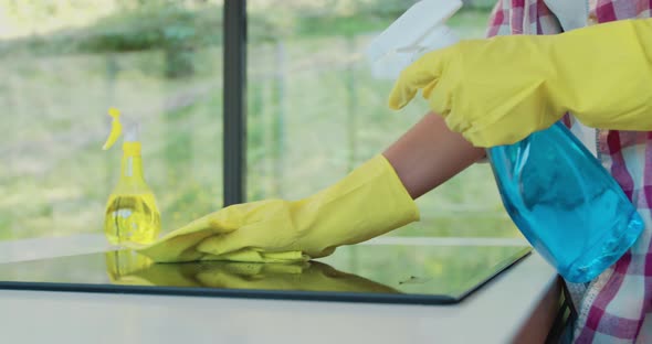 Cleaning Cooktop Cooking Panel in Kitchen with Fat Remover Spray and a Duster By a Woman in Yellow