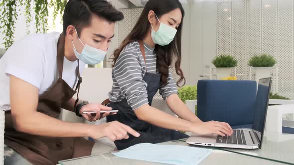 Asian couple in masks doing business calculations of restaurant and checking bills