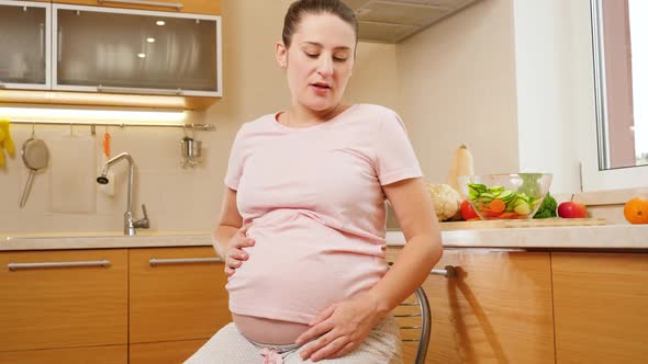 Young Pregnant Woman Suffering From Pain in Abdomen Sitting and Resting on Chair on Kitchen
