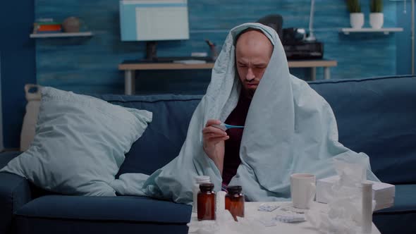 Ill Man in Blanket Measuring Temperature with Thermometer