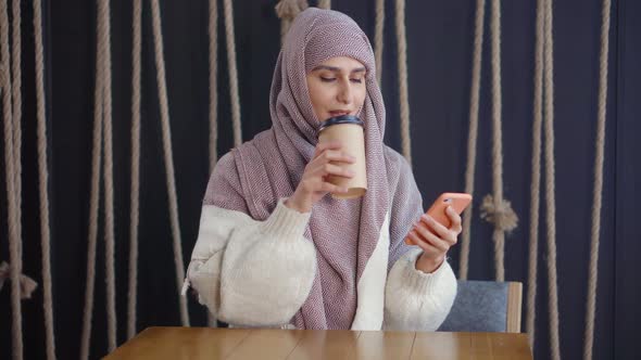 Arabic Woman Is Typing Sms in Smartphone, Sitting in Cafe with Carton of Coffee