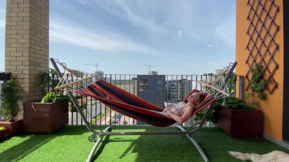 Rest in the City. Woman in Bikini Relax on Hammock on Terrace