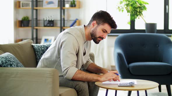 Man with Bills Counting on Calculator at Home