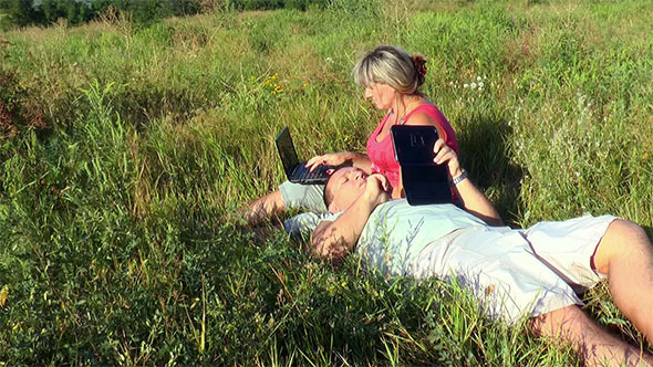 Couple on Meadow With Laptop and Tablet