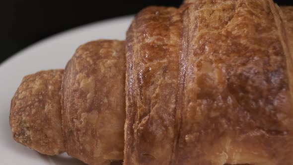 Croissant on white plate rotating in front of camera on black background