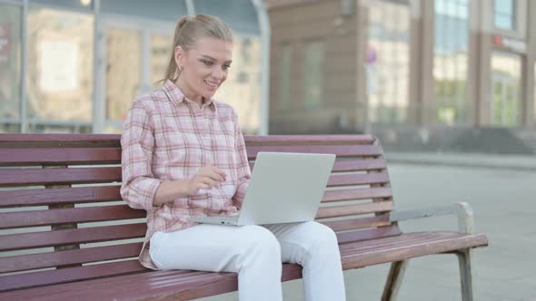 Young Woman Celebrating Success on Laptop While Sitting Outdoor on Bench