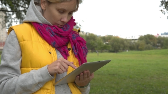 Woman In Yellow Vest Using Tablet Pc In The Park