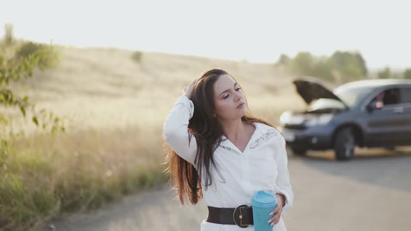 Girl with Cup in Hand Corrects Hair Talks and Looks Around at Broken Car