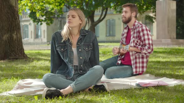 Portrait of Young Blond Caucasian Woman Enjoying Music As Bearded Man Playing Ukulele at the