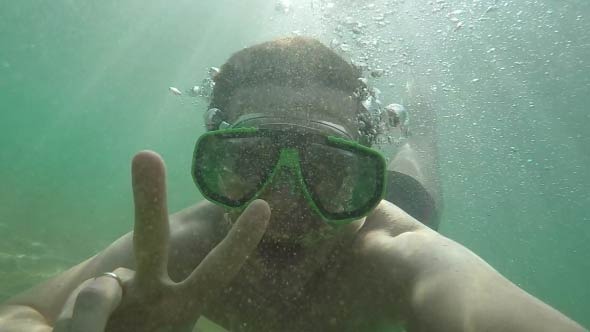 Man Smiling And Shows Peace Sign Under Water 