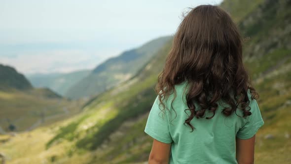 Cinematic back view of a girl looking out over a green valley of mountains. alt