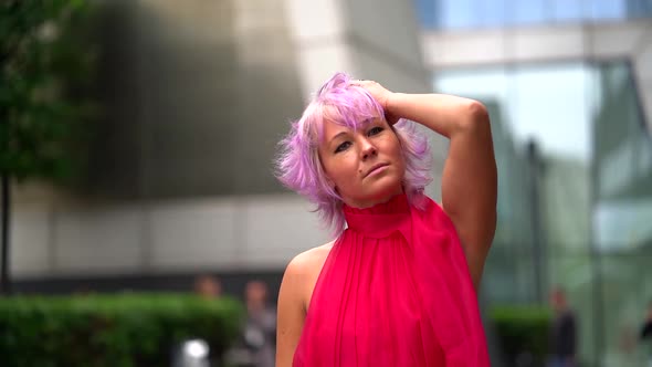 Extravagant Woman with Pink Hair, Dressed Red Gown Is Walking in City Streets