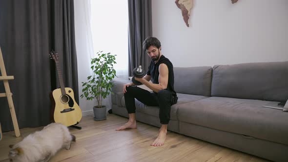 Man Doing Exercises with Dumbbells at Home in the Living Room on the Couch Showing Biceps