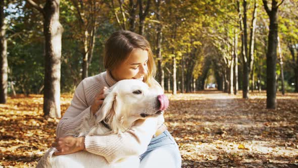 Young Gorgeous Lady is Sitting on Walkway of Autumn Park Smiling and Stroking Her Funny Dog Labrador