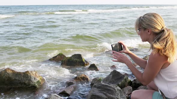 Woman Photographs the Sea Landscape on the Phone While Sitting on the Stones