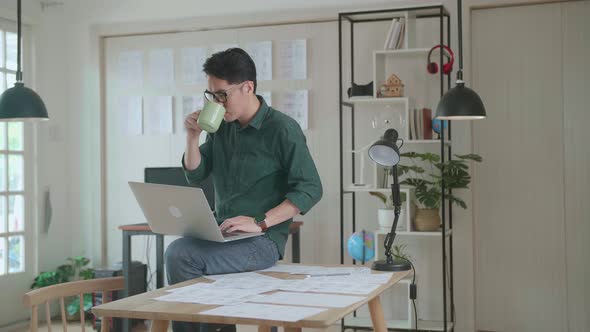 Creative Designer Sits On His Desk Holds Laptop On The Knees Drinks Coffee While Working