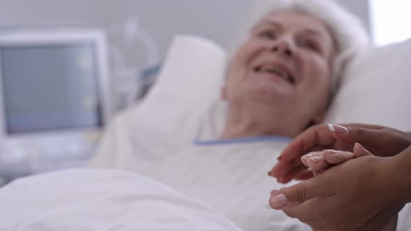 Senior Lady Holding Hands with Nurse in Hospital Ward