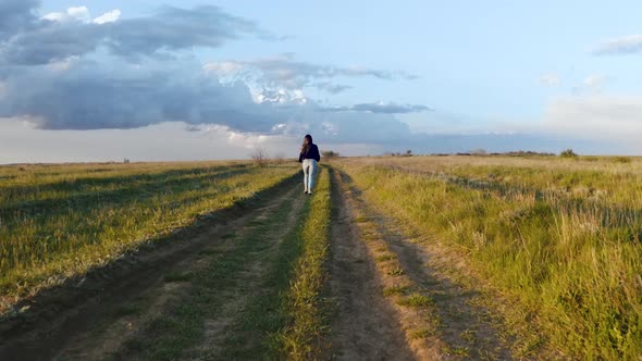 Young Woman Runs on the Field Road Near Water During Beatiful Sunset Aerial Shot