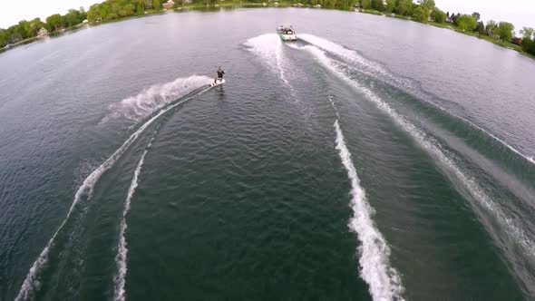 Aerial birds-eye drone view of a man wakeboarding behind a boat.