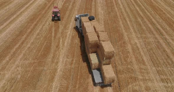 Tractor loading Hay bales onto a trailer, Aerial view.