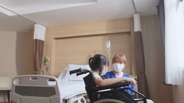 Asian nurse wear mask, taking care of kid patient sit on wheelchair in recovery room in hospital.