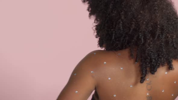 Mixed Race Black Woman with Curly Hair Covered By Crystal Makeup on Pink Background in Studio