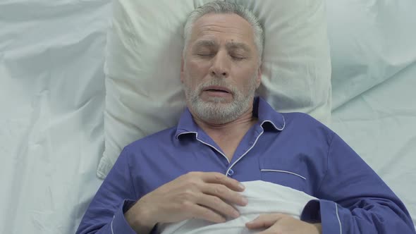 Senior man loudly snoring and puffing in bed, sleeping problems at old age