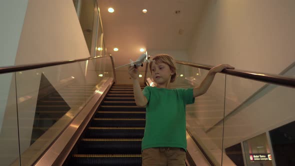 Little Boy Moves Down the Escalator Holding White Toy Airplane in His Hand. Freedom Concept