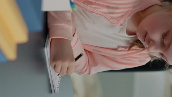 Vertical Video Portrait of Schoolgirl Using Notebook and Pen to Write Homework