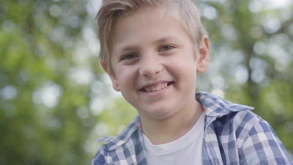 Close-up Portrait of Cute Handsome Boy in Checkered Shirt Looking Into Camera Sitting in the Park