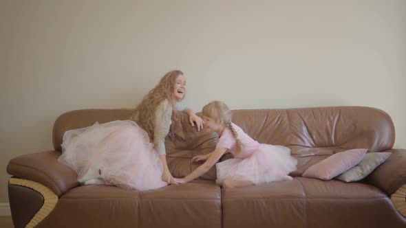 Young Caucasian Mother and Her Cute Little Girl in the Same Skirts Jumping on the Leather Sofa