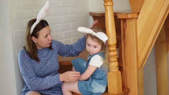 a Mother Soothes Her Crying Daughter on the Wooden Stairs of the House