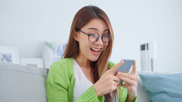 Asian beautiful woman wear eyeglass, feeling excited after check on mobile phone in house.