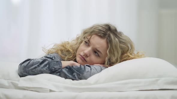 Young Sleepy Caucasian Woman Opening Eyes Looking Around and Hiding Under Blanket