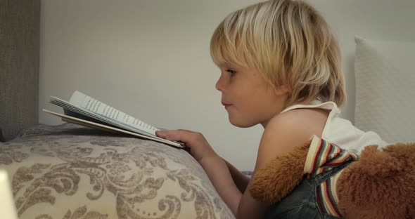 Little Boy Reading a Book Before Bedtime in His Bed on Evening