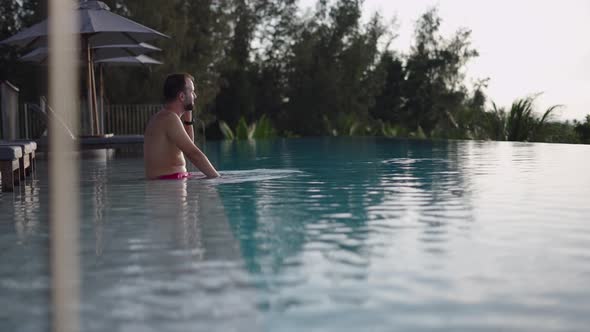 Spanish Adult Man Talking on Phone Enjoying the Sunset View From the Infinity Pool in Rooftop Hotel