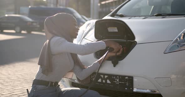 Black Muslim Girl Charging Electro Car at the Station