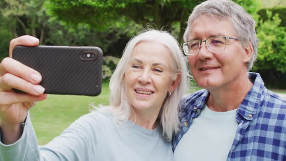 Animation of caucasian senior couple embracing in garden, taking selfie