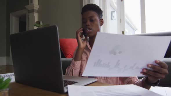 African american woman holding a document talking on smartphone while working from home